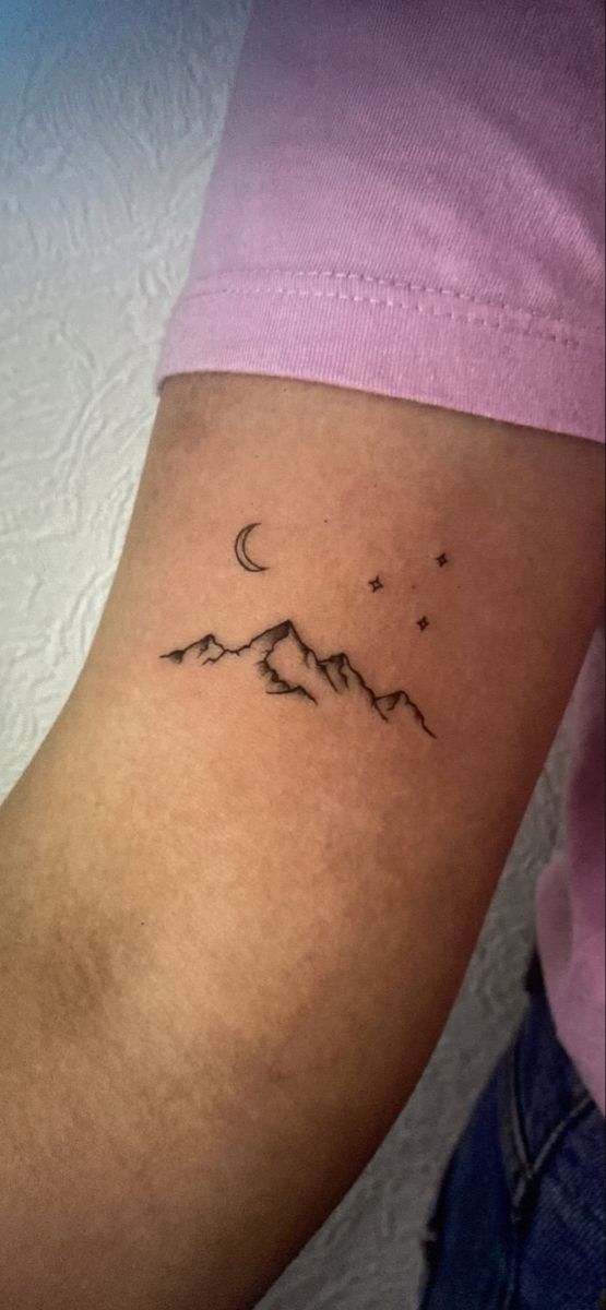 a woman's arm with a small mountain and stars tattoo on the left side