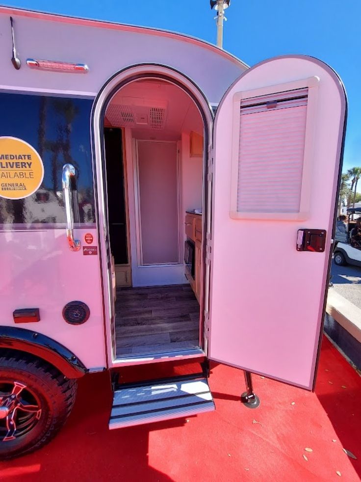 a pink trailer with its door open on a red carpeted floor and other vehicles in the background