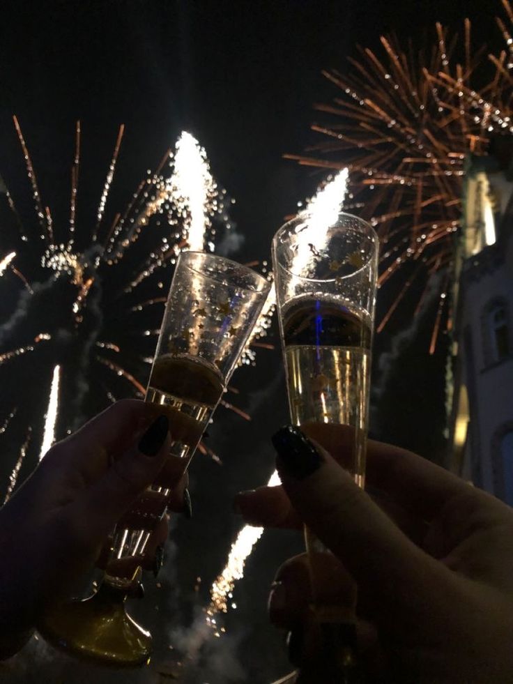 two people toasting with champagne in front of fireworks on the night sky and clock tower