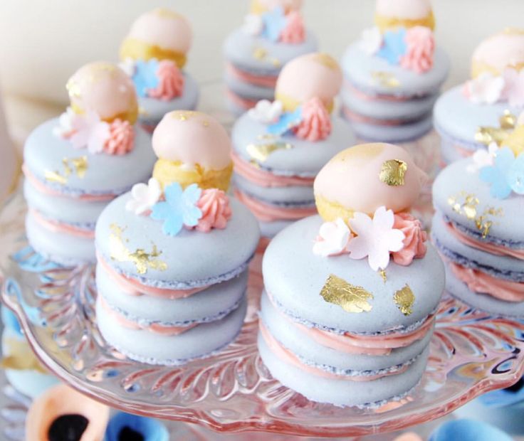 there are many blue and pink macaroons on the glass platter with gold leaf decorations