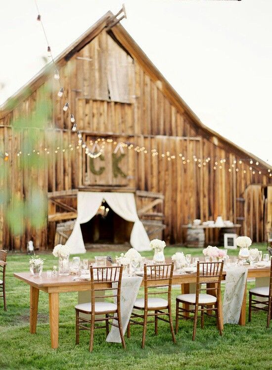 an outdoor wedding reception setup in front of a barn with lights strung from the roof