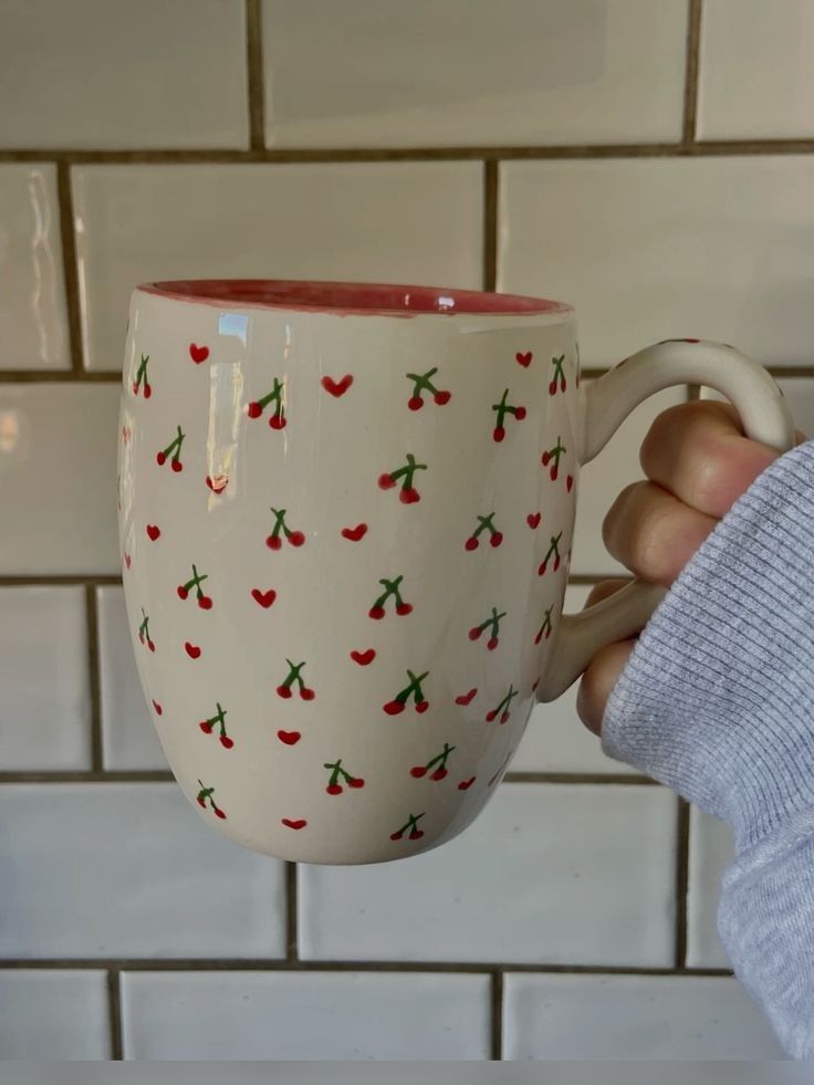 a person holding a coffee cup with cherries on it in front of a tiled wall