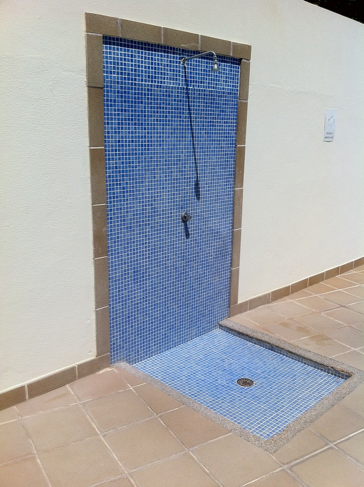 a blue tiled shower stall in a white walled room with tile flooring and walls