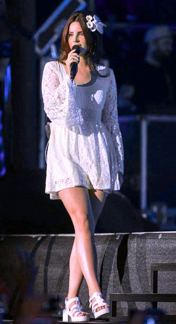 a woman standing on top of a stage with a microphone in her hand and wearing white shoes