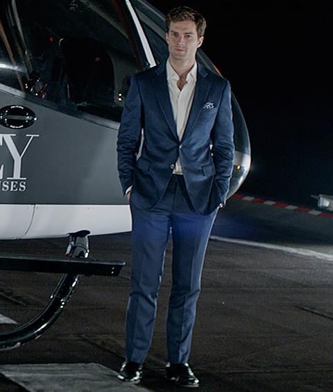 a man in a suit standing next to a gray and white helicopter with the words grey enterprises on it