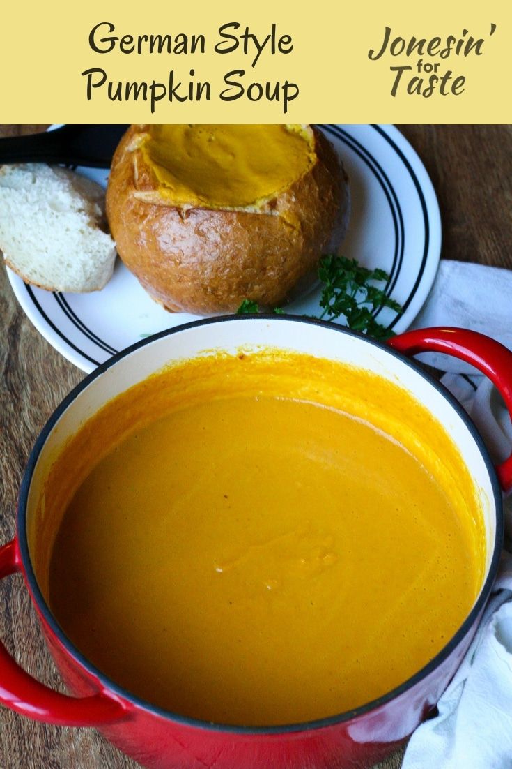 a red pot filled with soup next to bread on top of a wooden table in front of a white plate