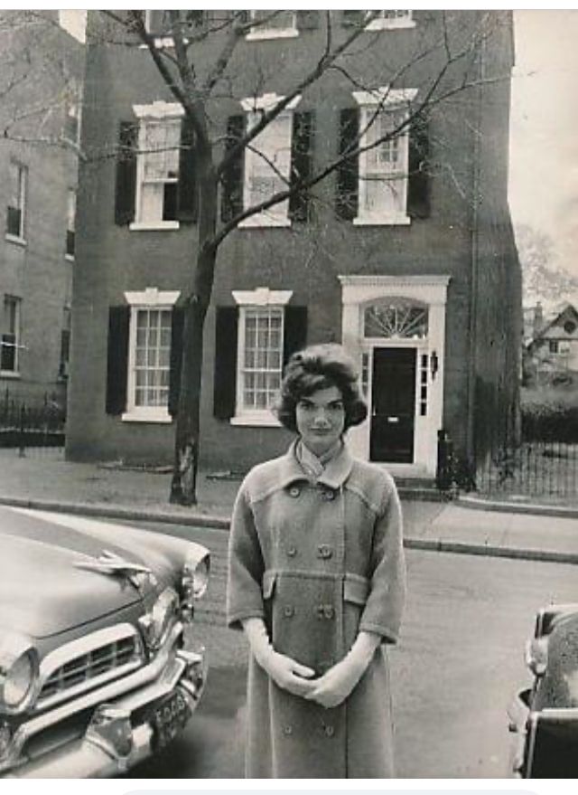 an old black and white photo of a woman standing in front of a car on the street