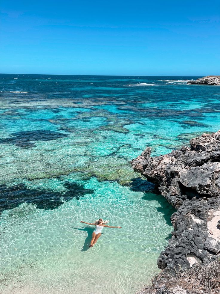 a woman is swimming in the clear blue water near some rocks and coral reefes