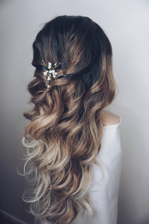 a woman with long wavy hair and a flower in her hair is seen from the back