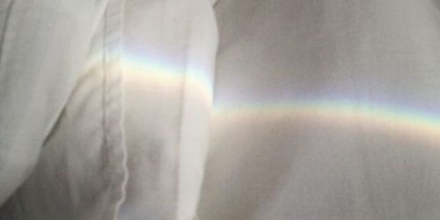 a person wearing a white shirt with a rainbow in the background