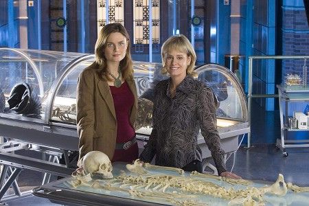 two women standing in front of a display case with skulls and bones on the table