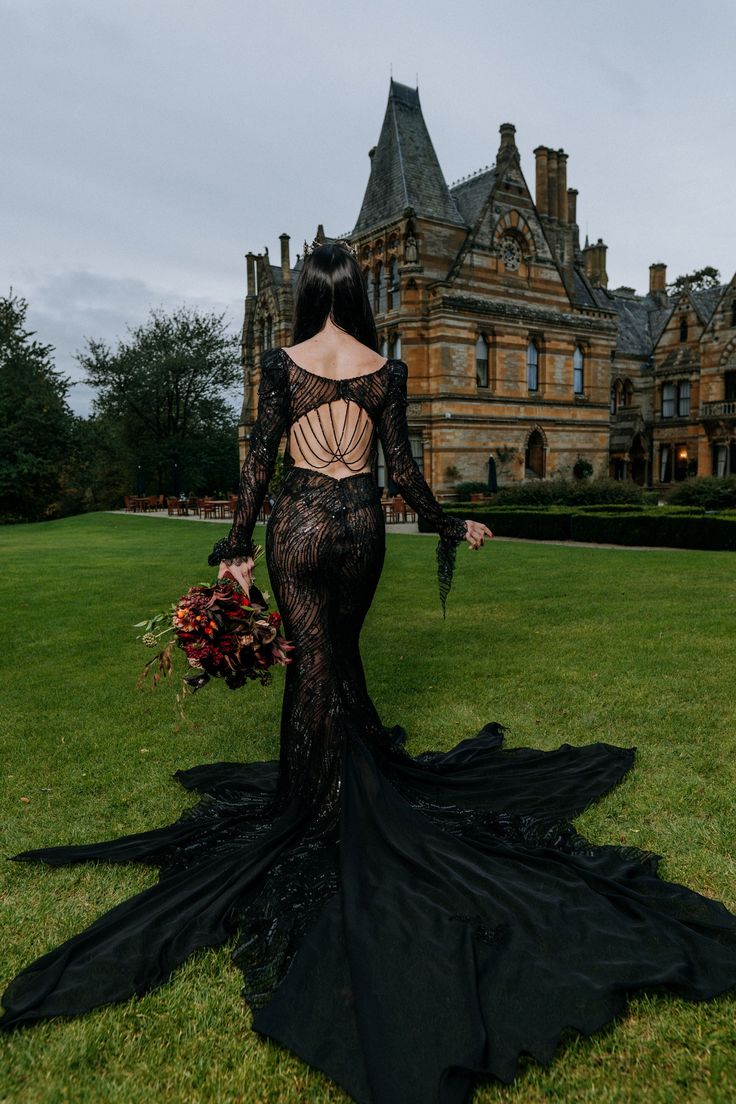 a woman standing in front of a large building wearing a black dress with open back