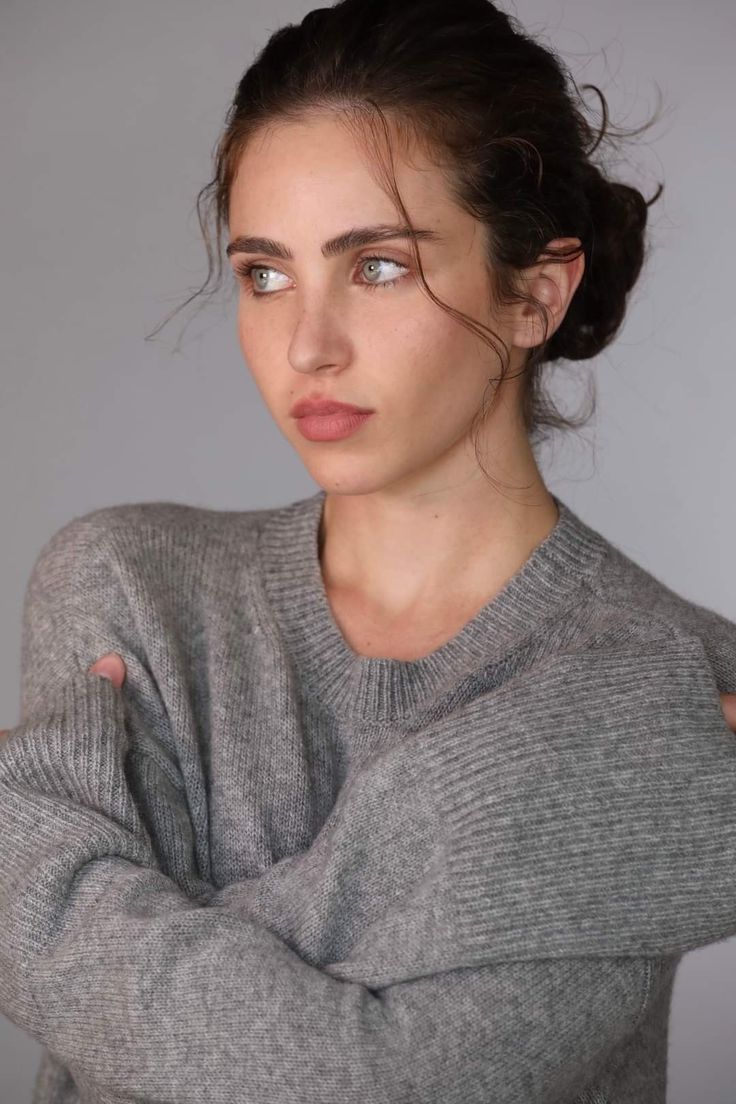 a woman with her arms crossed looking at the camera while wearing a gray sweater and jeans