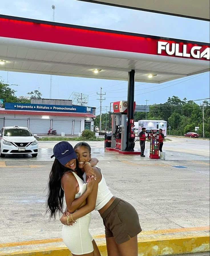 two women hugging each other in front of a gas station