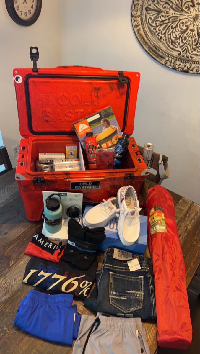 an open red suitcase sitting on top of a wooden table filled with clothing and other items