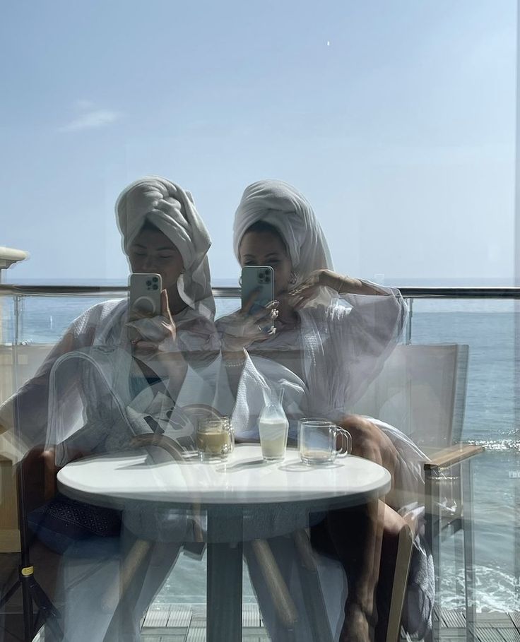 two women sitting at a table with their cell phones in front of them, both wearing headscarves