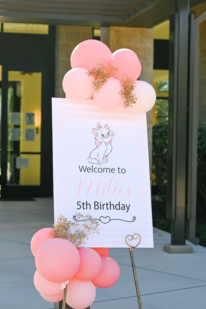 a welcome sign with pink balloons in the foreground and an image of a dog on it