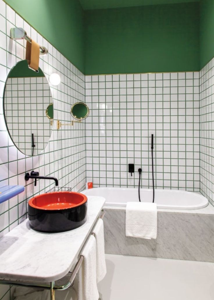 a bathroom with green and white tiles on the walls, a red bowl in the middle