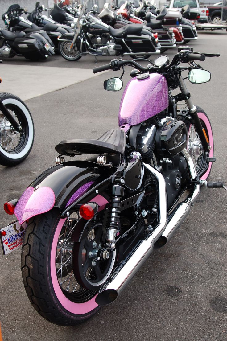 a pink and black motorcycle is parked in a parking lot with other motorcycles behind it