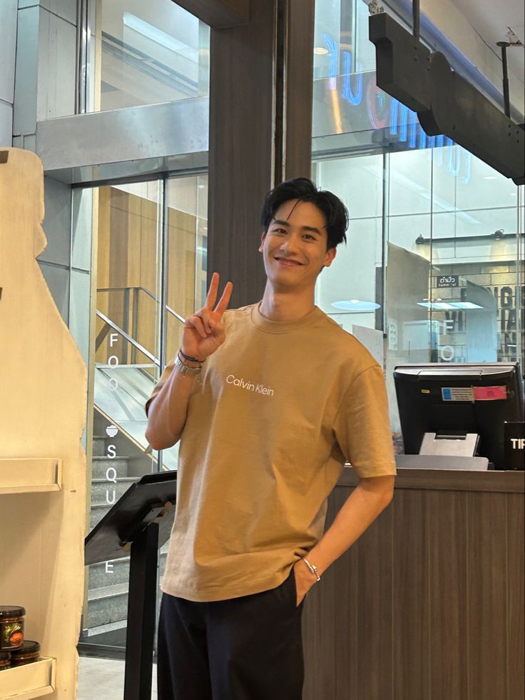 a young man standing in front of a counter giving the peace sign with his hand