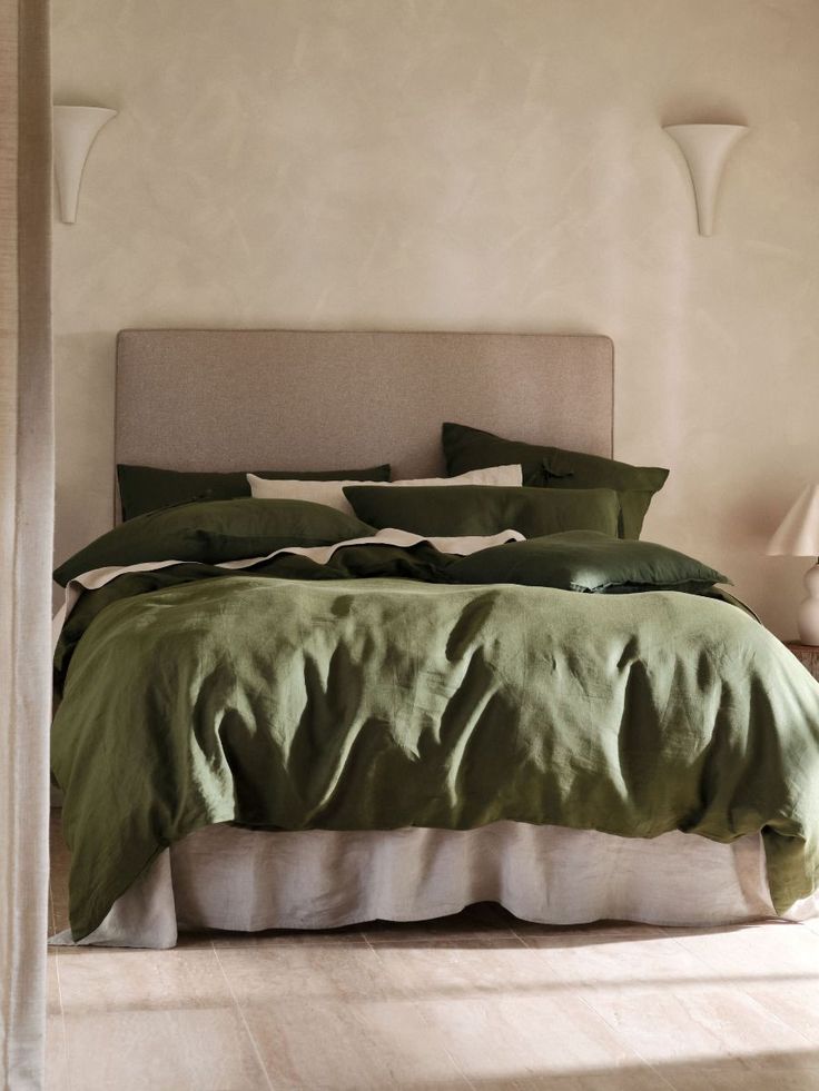 a bed with green sheets and pillows in a bedroom next to two lamps on either side of the bed