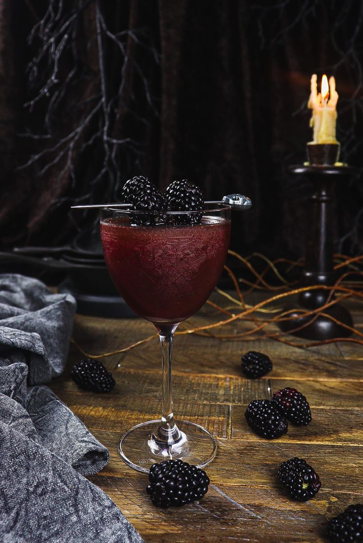 a glass filled with blackberries on top of a wooden table next to a candle