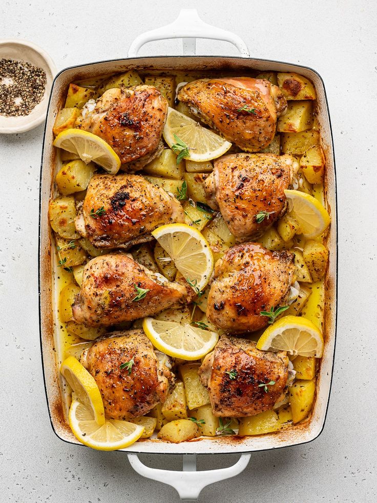 chicken with lemons, potatoes and herbs in a casserole dish on a white surface