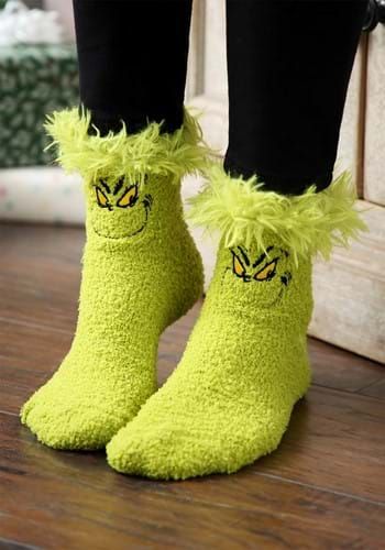 the legs and feet of a person wearing fuzzy green socks with yellow eyes, black leggings