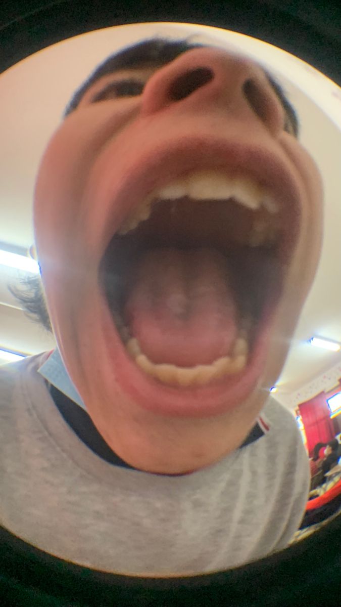 a man with his mouth wide open in front of a round mirror that is reflecting him