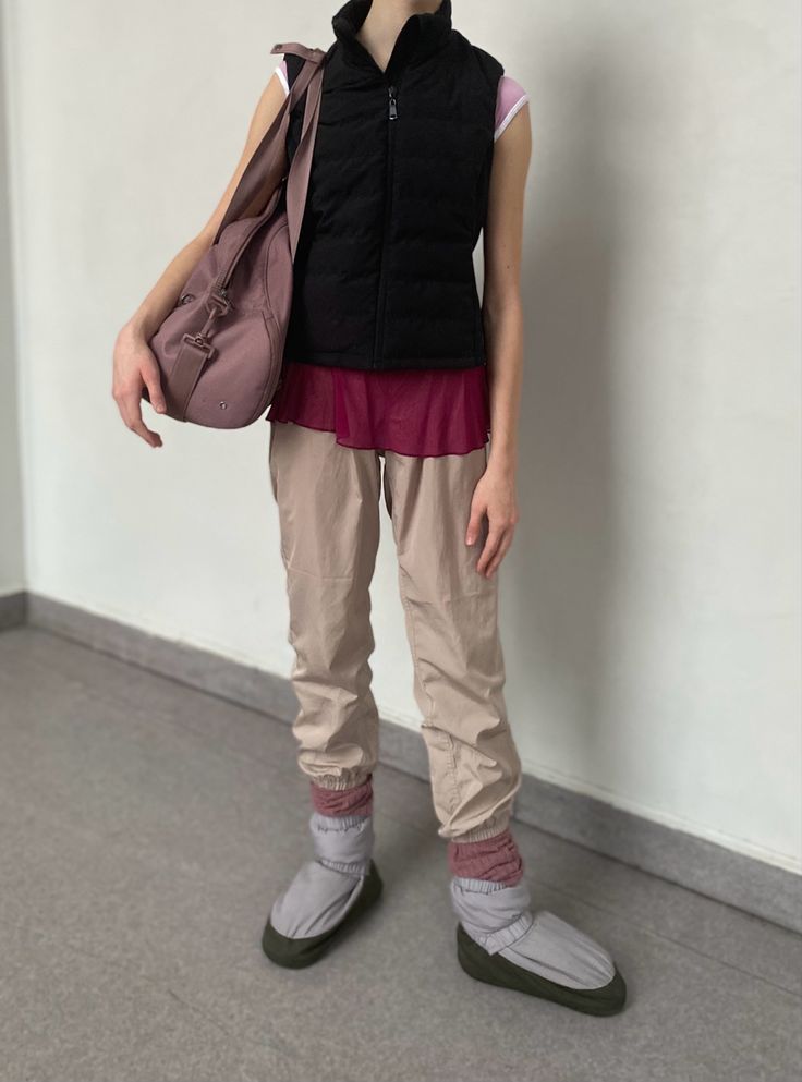 a woman standing in front of a white wall holding a purse and looking at the camera