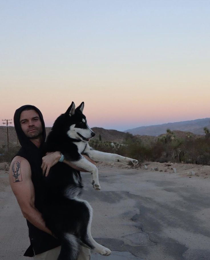 a man holding a husky dog on his back in the middle of an empty road