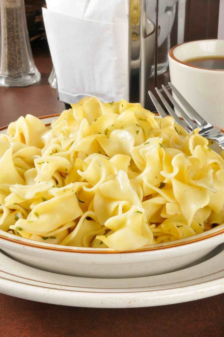 a white plate topped with pasta on top of a wooden table next to a cup of coffee