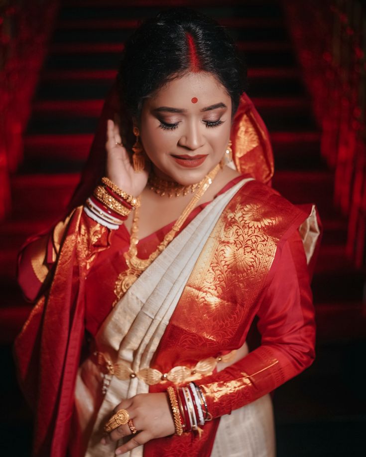 a woman in a red and white sari holding her hand up to her ear