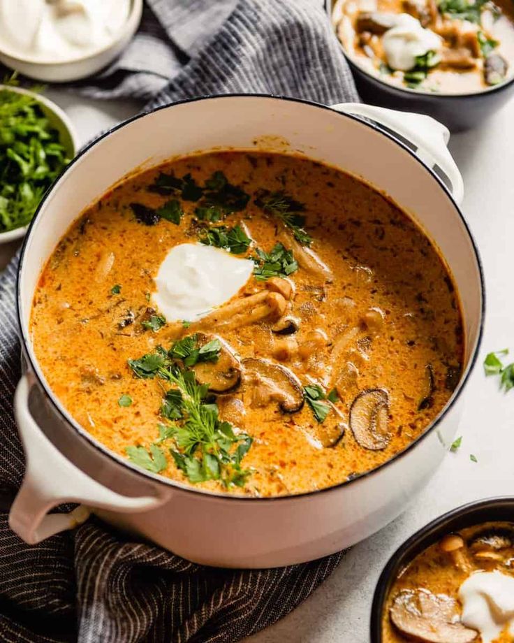 a bowl of soup with mushrooms, sour cream and parsley on the side next to other dishes