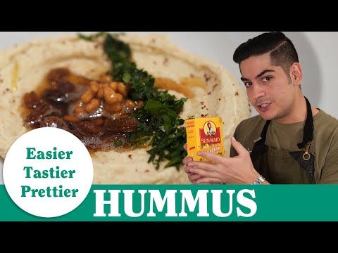 a man holding up a carton of hummus next to a plate of food