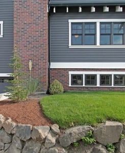 an apartment building with grass and rocks in the foreground, next to a stone wall