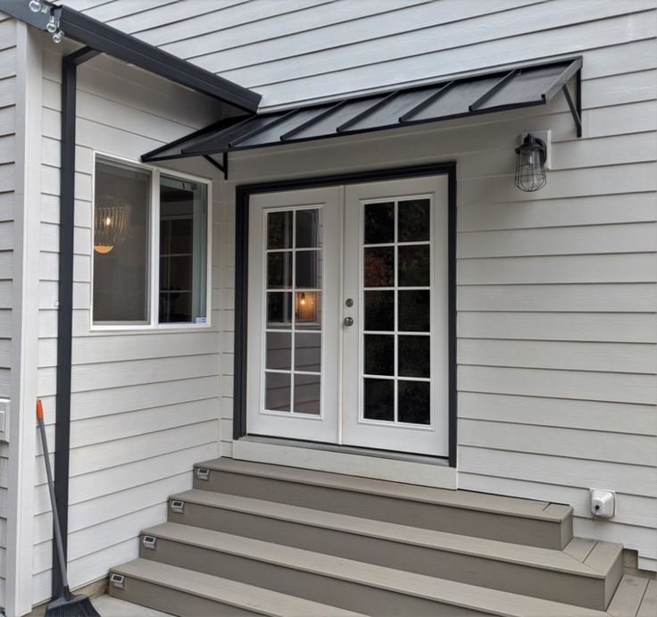 a white house with steps leading up to the front door and entry way that has glass doors on both sides