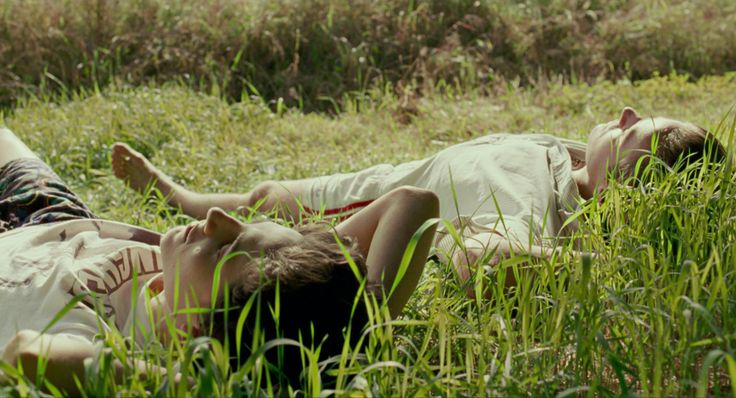 two people laying on the ground in tall grass