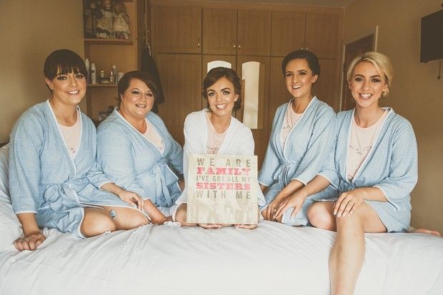 four women in blue robes sitting on a bed holding a sign that says, be nice to the nurses