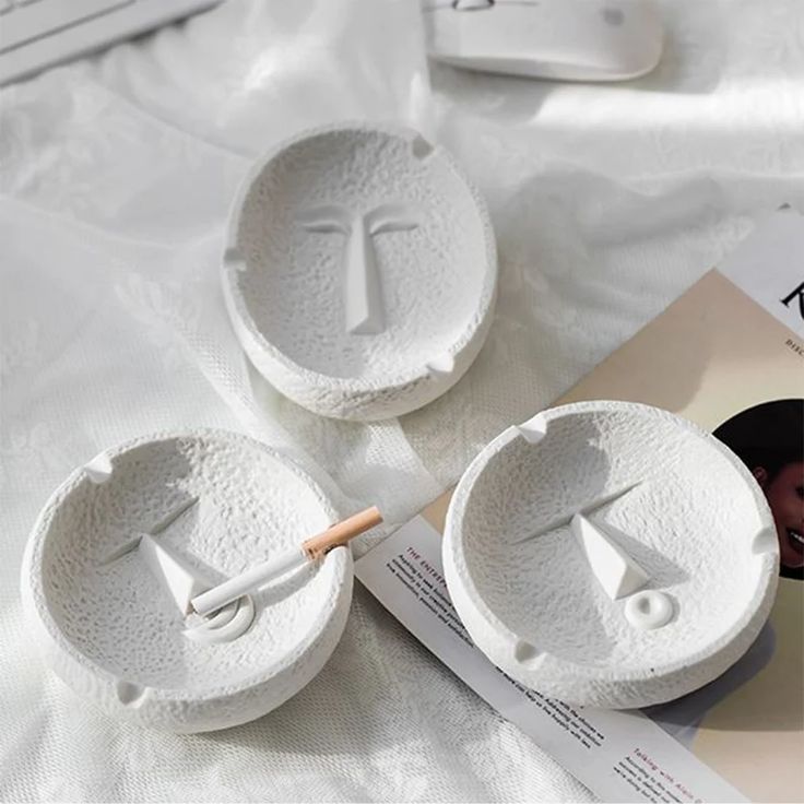 three white bowls sitting on top of a bed next to a magazine and remote control