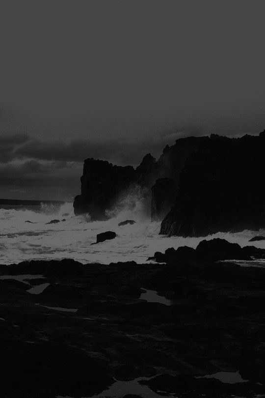 a black and white photo of waves crashing on the rocks at night with dark clouds