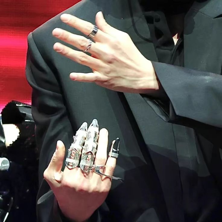 a man in a black suit holding his hands out with two rings on each hand