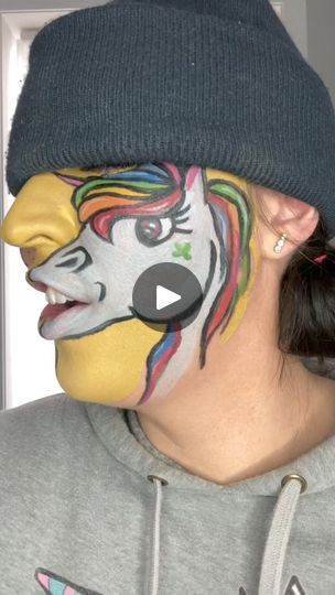 a woman with her face painted like a clown wearing a beanie and grey sweatshirt