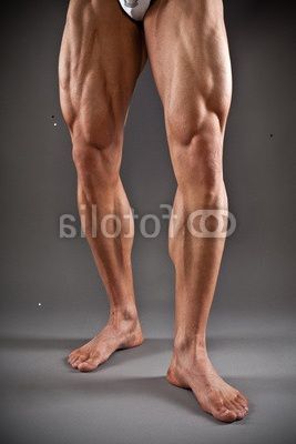 the legs and ankles of a man with no shirt on, in front of a gray background