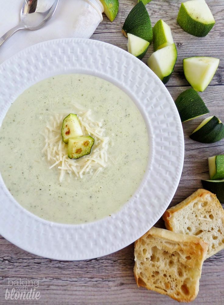 a white plate topped with soup next to slices of bread and cucumber wedges