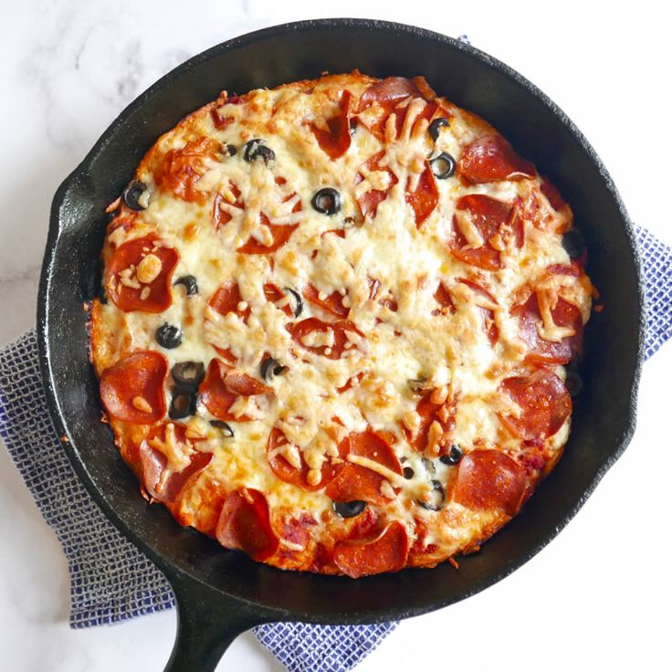 a pepperoni and olive pizza in a cast iron skillet on a blue towel