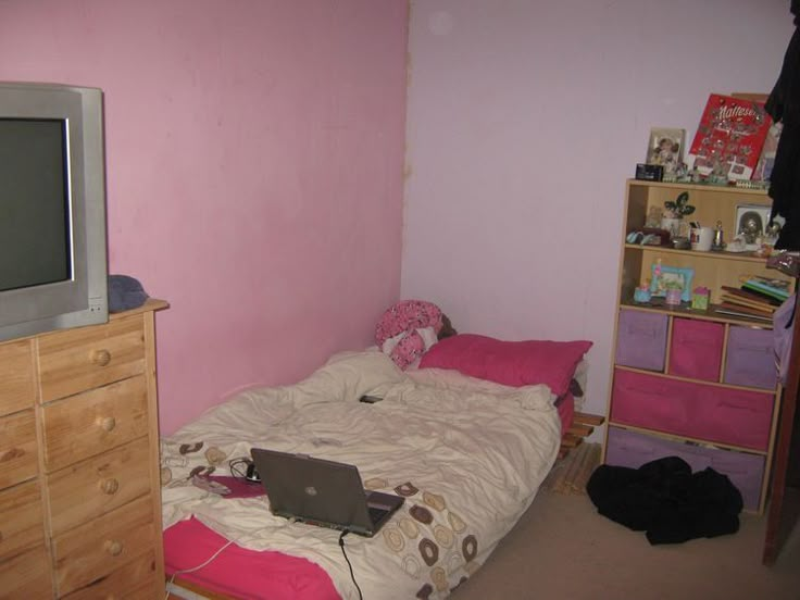 a bedroom with a bed, dresser and tv in the corner next to pink walls