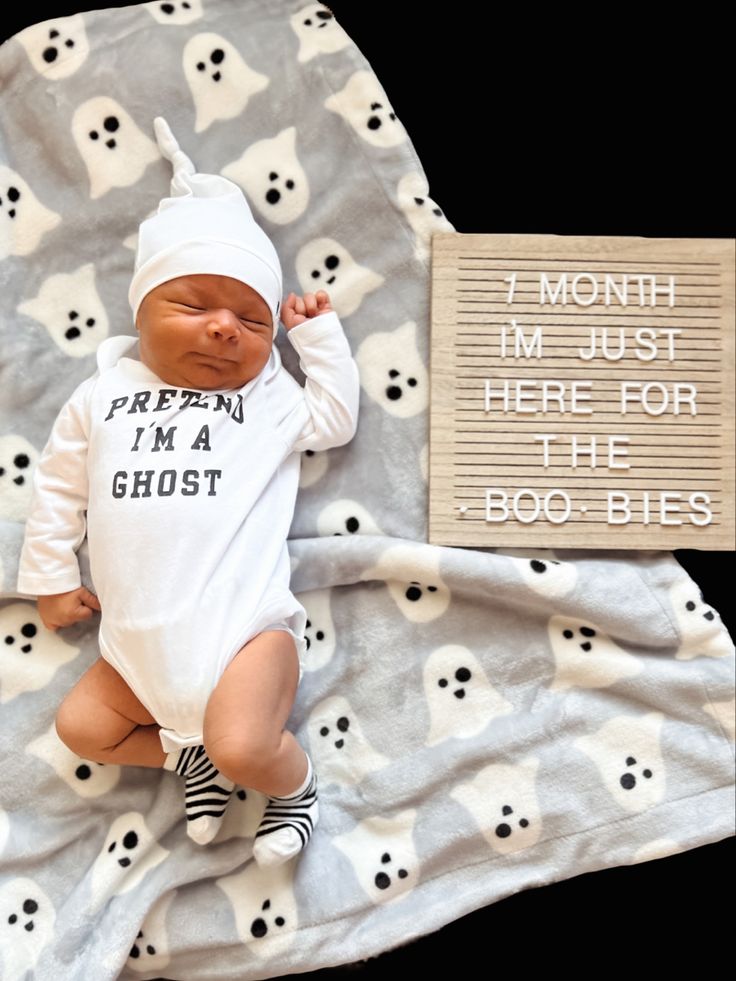 a baby laying on top of a blanket next to a sign that says i month im just here for the ghost