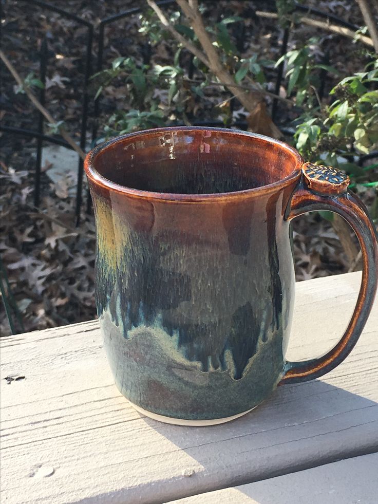 a brown and green mug sitting on top of a wooden table next to some bushes