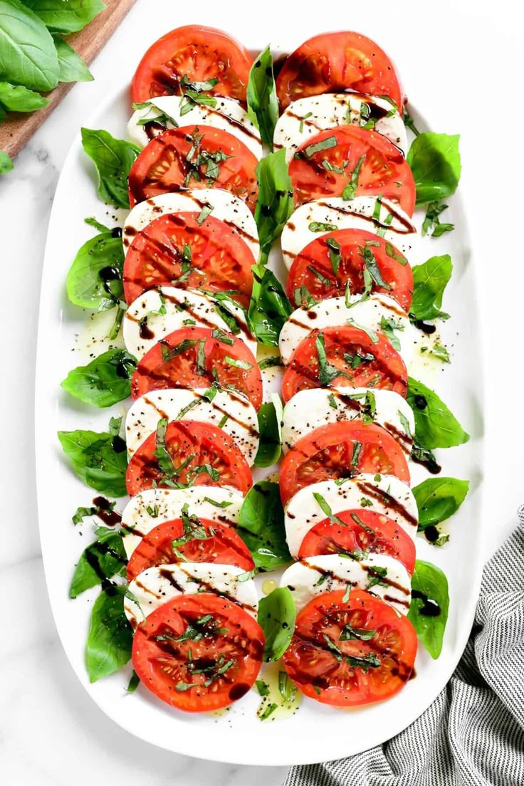 sliced tomatoes and basil on a white platter with fresh mozzarella sauce in the background